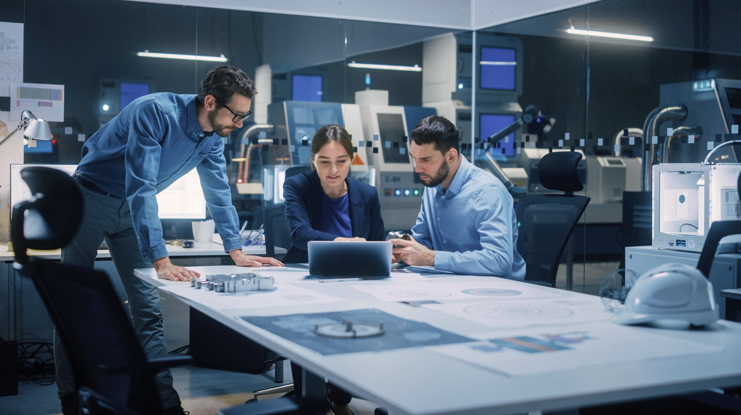 two men and a woman working in an office looking at a tablet device